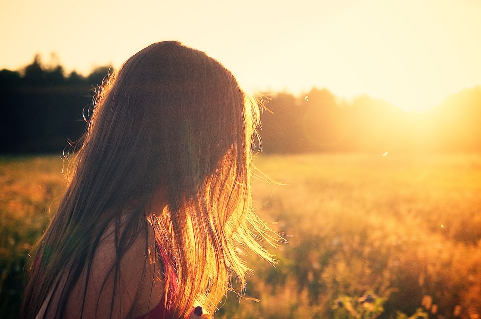 Kopf einer Frau mit wallendem Haar in einem Feld bei Sonnenuntergang. Bild zum Thema: Schönheits-OPs: Braucht Schönheit Nachhilfe?