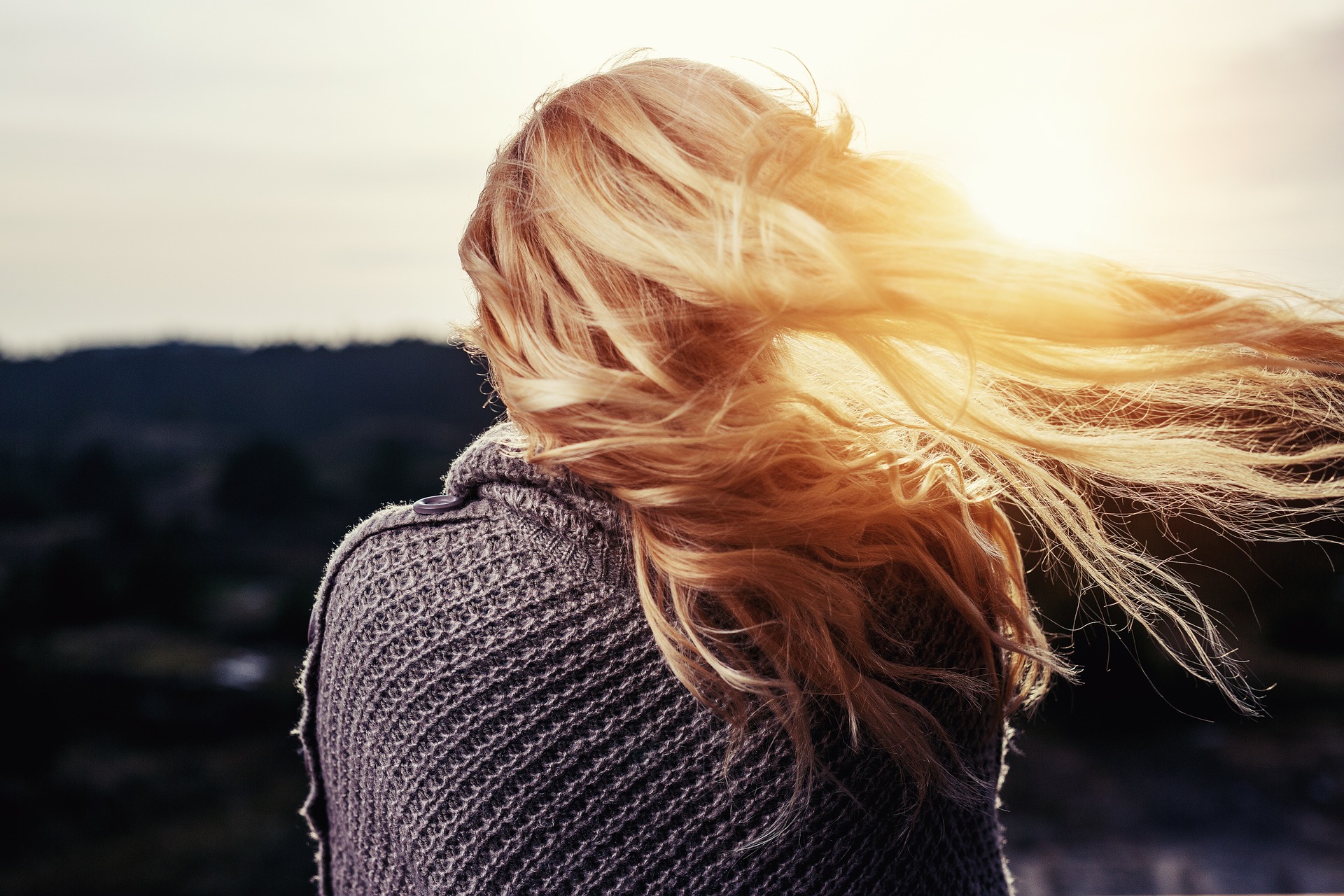 Frau im Pullover bei Sonnenuntergang mit dem Rücken zugewandt. Bild zum Thema: Angst vor den Risiken der Schamlippenkorretur
