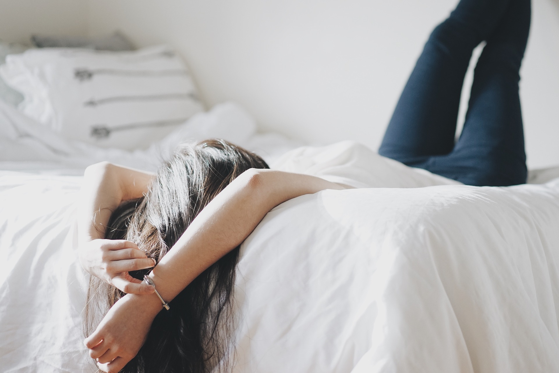 Eine Frau liegt bekleidet auf einem Bett, die Füße an der Wand und die Hände hinter dem Kopf. Bild zum Thema: Eigenfett – Vom Feind zum Wundermittel