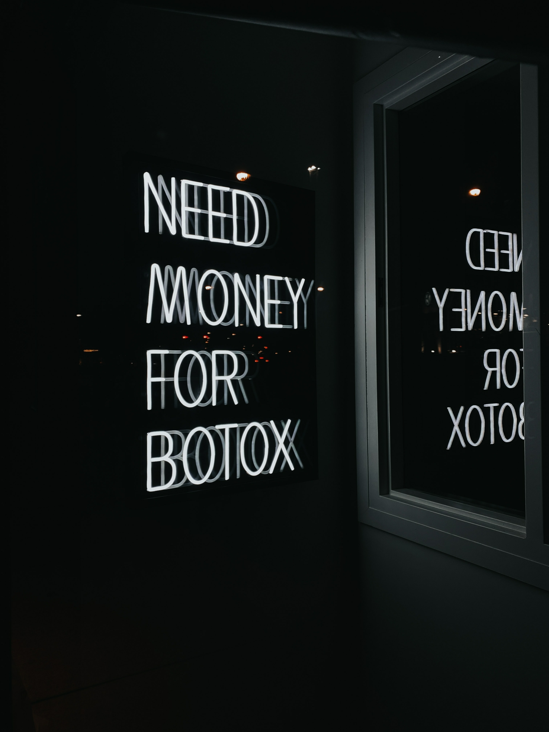 Leuchtschrift mit der Aufschrift: "Need money for Botox", spiegelt sich im Schaufenster
