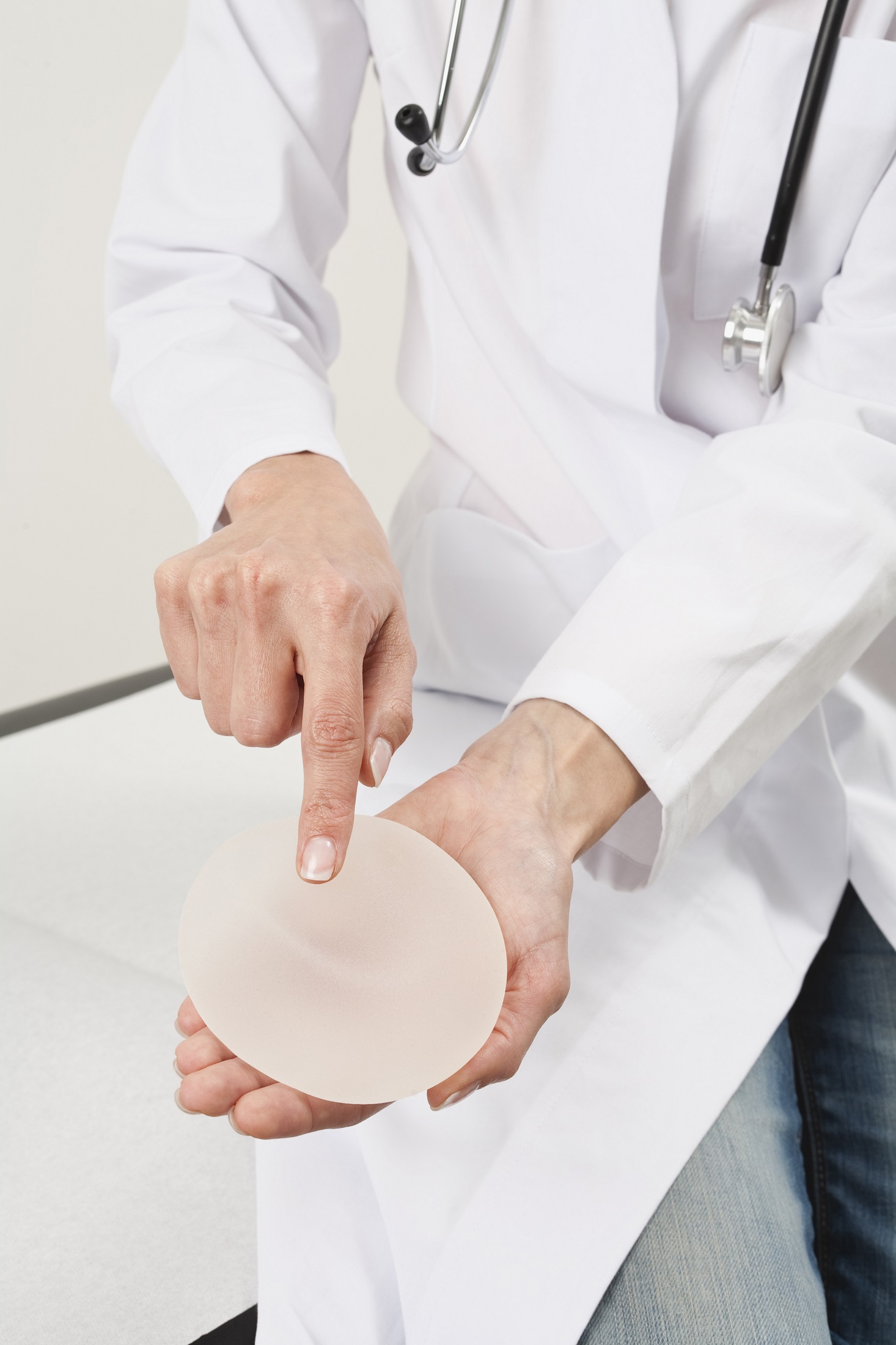 Brustimplantat auf der Hand des Arztes, die auf ihn zeigt. Bild zum thema: Brustimplantate – Für immer? 