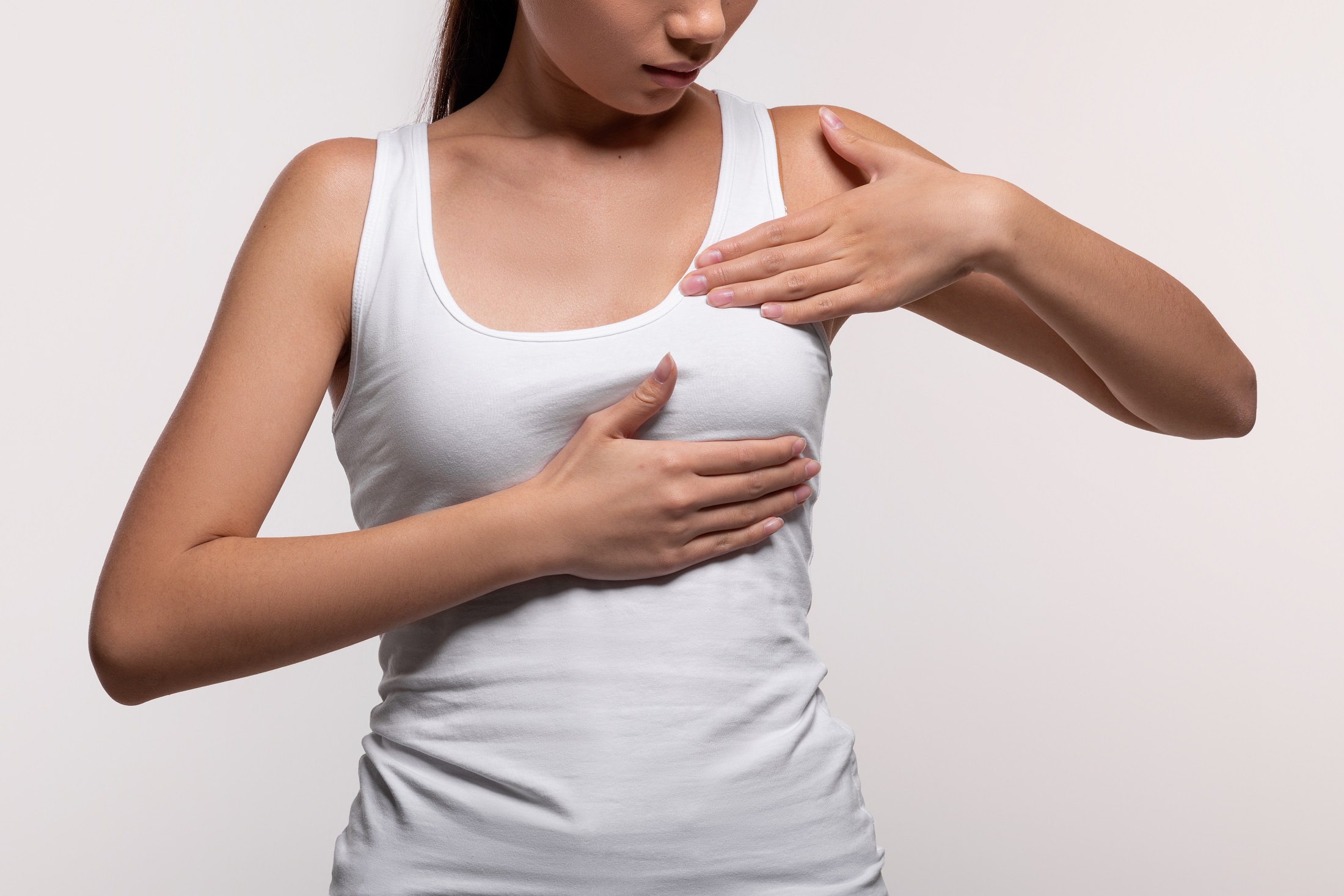 Eine Frau in einem weißen Tanktop betastet ihre Brust. Bild zum Thema: Kapselfibrose